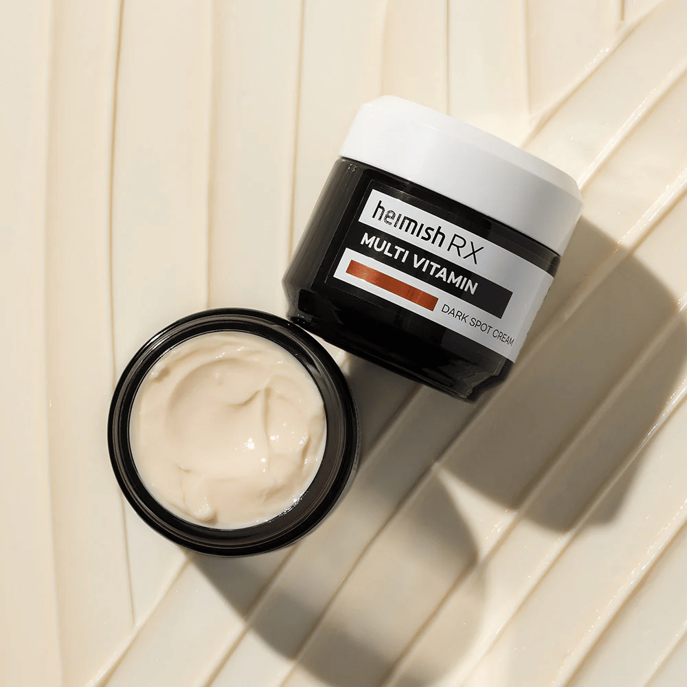 heimish RX Multi Vitamin Dark Spot Cream – en næringsrik ansiktskrem for å redusere mørke flekker og gi huden en jevnere tone. Kremens myke tekstur vises i en åpen boks med elegant emballasje.