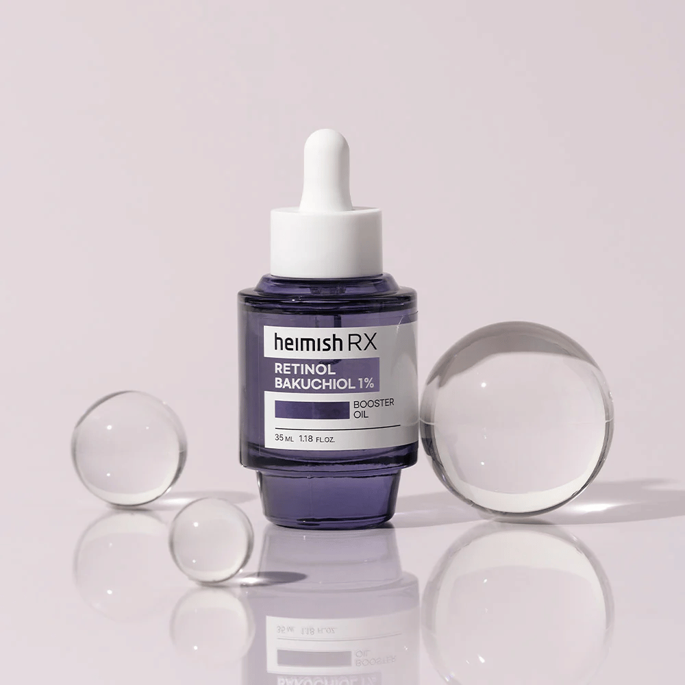 Heimish RX Retinol Bakuchiol Booster Oil 1% i en elegant lilla glassflaske med pipette. Oljen er plassert på en reflekterende overflate med glasskuler rundt, noe som gir en luksuriøs og moderne følelse.
