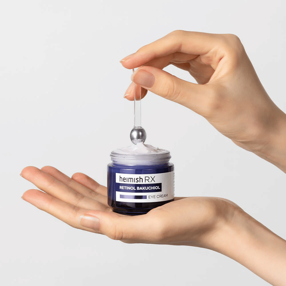 Heimish RX Retinol Bakuchiol Eye Cream i en elegant blå boks, løftes opp med en metallapplikator. En øyekrem med retinol og bakuchiol for å redusere fine linjer og gi en fastere hud.