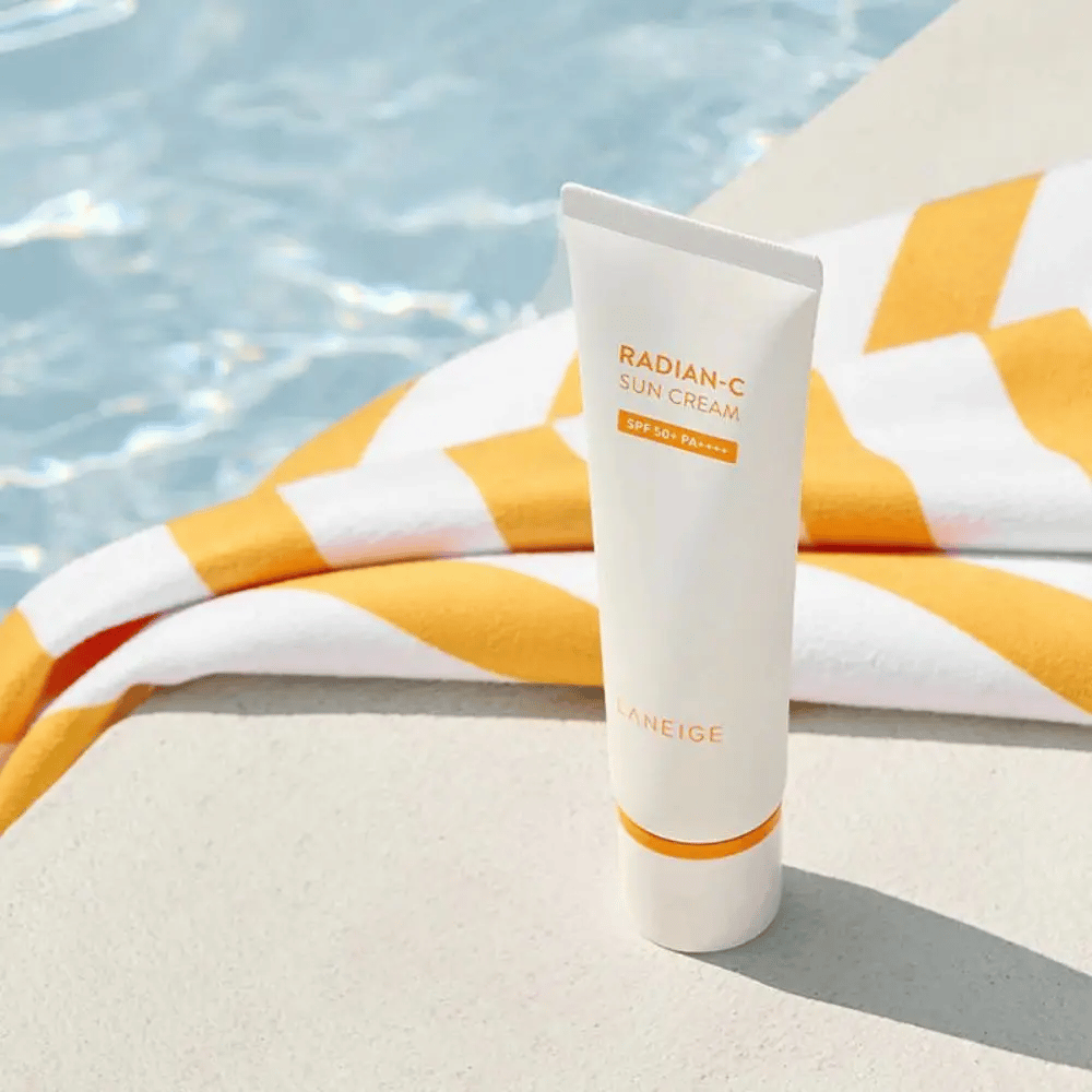 LANEIGE Radian-C Sun Cream står ved en bassengkanten med et gul- og hvitstripet håndkle i bakgrunnen.
