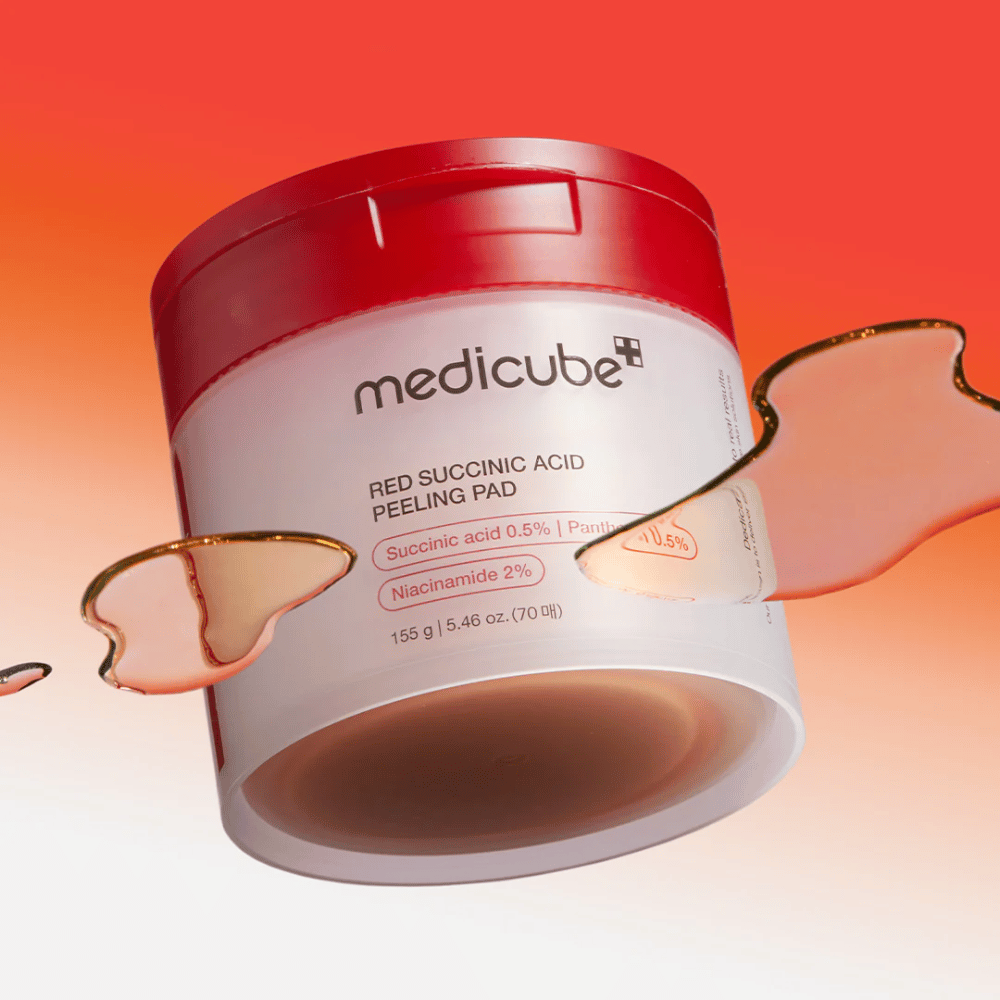 Medicube Red Succinic Acid Peeling Pad i en hvit og rød boks, plassert mot en gradientbakgrunn i rødt og oransje. Produktet inneholder succinsyre og niacinamid for eksfoliering og hudforbedring. Flytende tekstur vises rundt boksen.