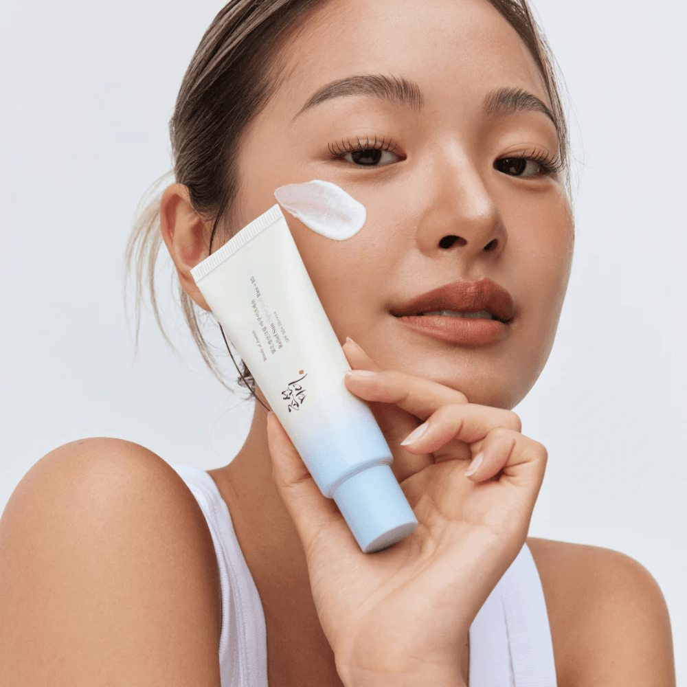 Kvinne holder Beauty of Joseon Relief Sun: Aqua-Fresh Rice + B5 solkrem og viser dens kremete konsistens på kinnet. En lett solbeskyttelsesprodukt som fukter og beskytter huden med SPF 50+ PA++++.
