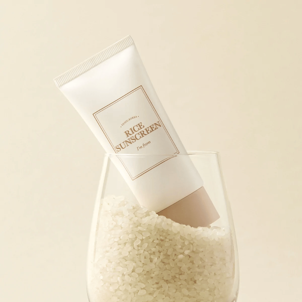 Tube med "I'm from" Rice Sunscreen, SPF50+ PA++++, plassert i et glass med riskorn.