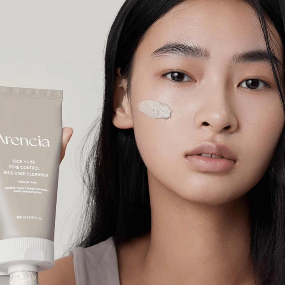 Modell som holder Arencia Rice + LHA Pore Control Rice Cake Cleanser med påført produkt på kinnet, illustrerer mild men effektiv porerens for daglig bruk.