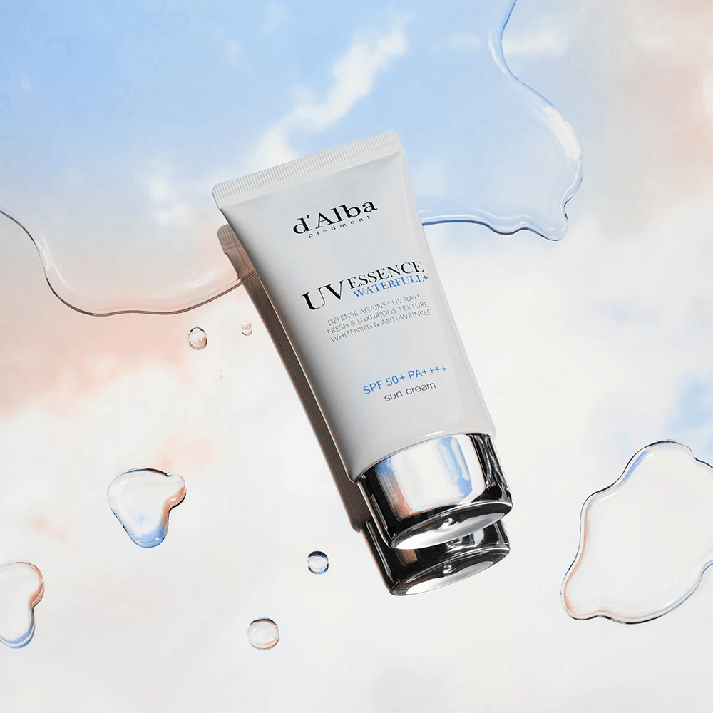 Produktbilde på d'Alba UV Essence Waterfull+ Sun Cream med SPF 50+ PA++++, plassert mot en bakgrunn med vannsprut og blårosa himmel – symboliserer lett og fuktighetsgivende solbeskyttelse.