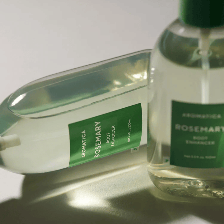 To AROMATICA Rosemary Root Enhancer-flasker med transparent beskyttelseshette og grønn etikett. Nærbilde som fremhever produktets premiumdesign og naturlige hårpleiekonsept.