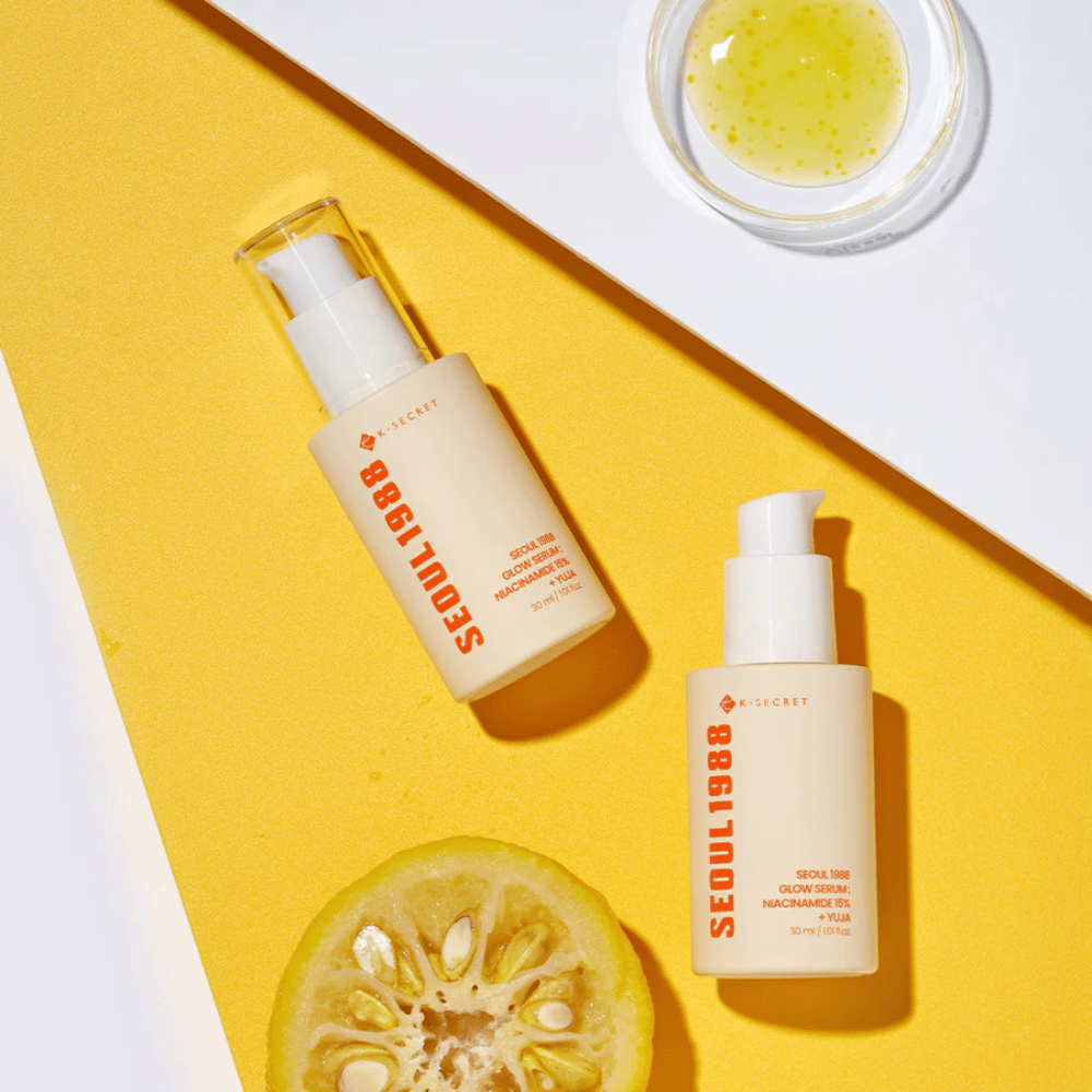 To flasker Seoul 1988 Glow Serum plassert på gul bakgrunn sammen med en skål med gult serum og en halvert sitrusfrukt.