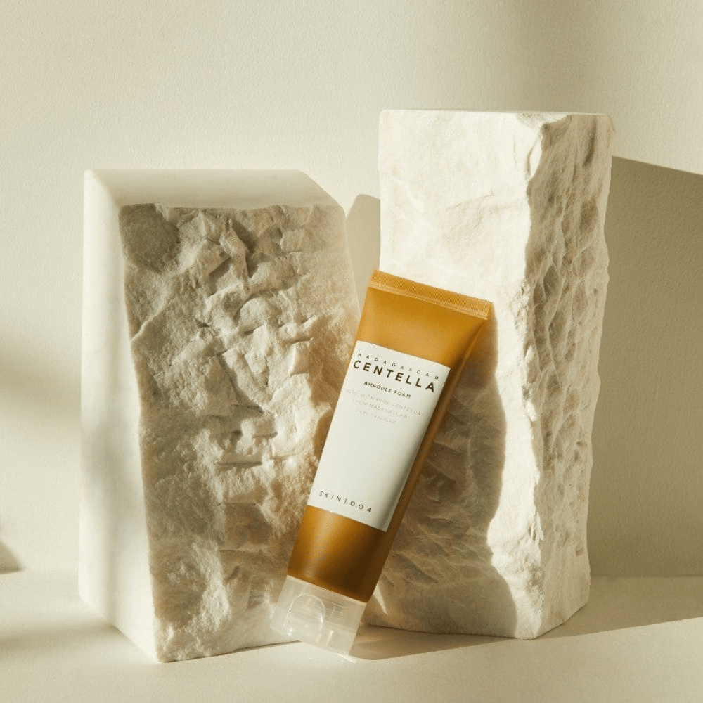 SKIN1004 Madagascar Centella Ampoule Foam stående mot lyse steinblokker i naturlig sollys, med sitt brunhvite tubedesign og elegant minimalisme.