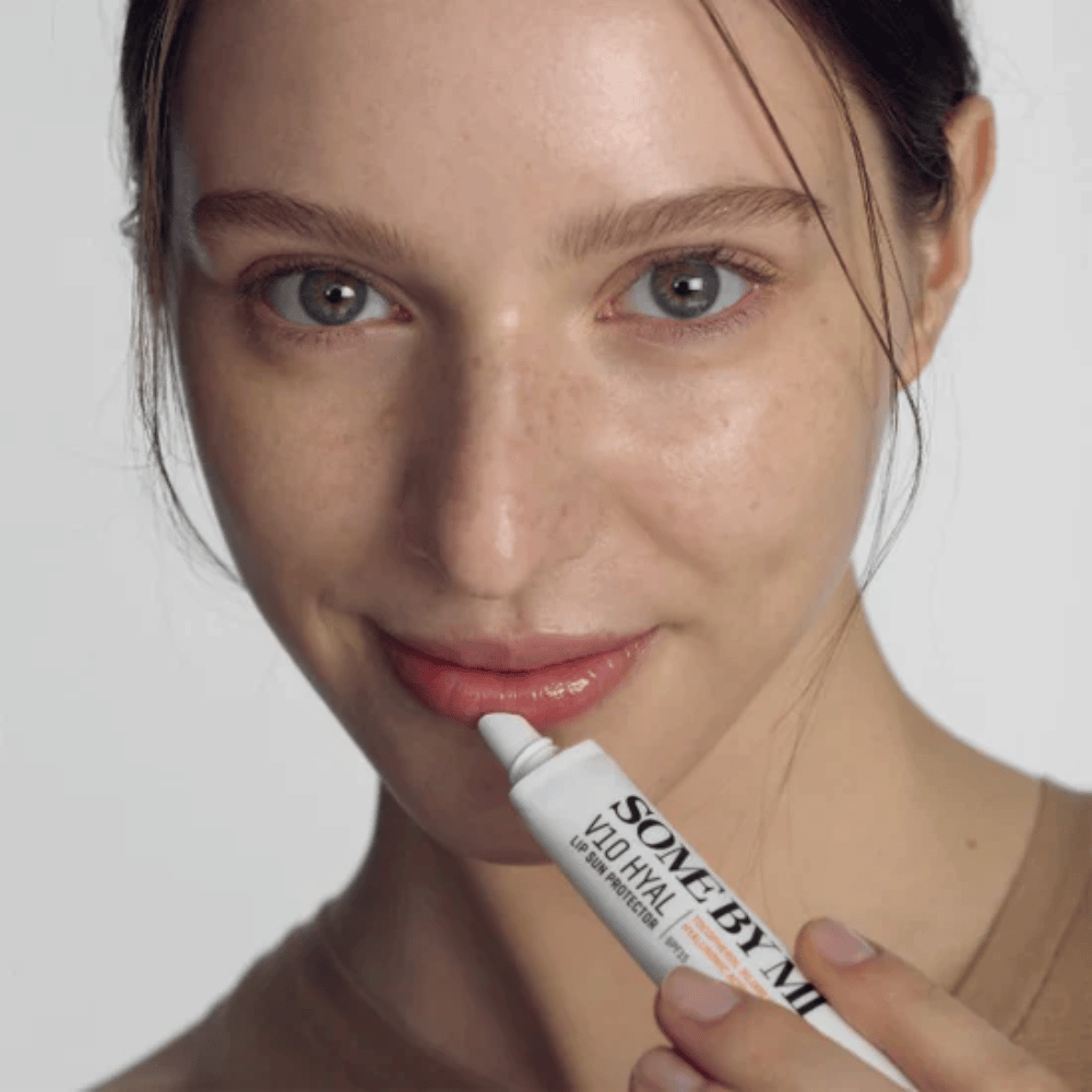 En kvinne holder i en tube V10 Hyal Lip Sun Protector SPF15 7ml leppebalsam for solbeskyttelse og fuktighet, av SOME BY MI.
