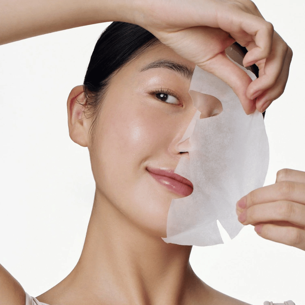 Dette bildet viser en person som bruker en ansiktsmaske, spesifikt "Galactomyces Glutathione Daily Mask" fra Some By Mi. Masken lysner huden og gir en strålende glød samtidig som den pleier og fukter huden i dybden, takket være ingredienser som glutation og vitamin C.