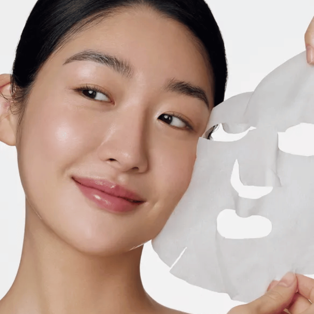 Bildet viser en person som bruker en ansiktsmaske, spesifikt en "Retinol Intense Daily Mask" fra Some By Mi. Masken er designet for daglig bruk og inneholder retinol for å forbedre hudens tekstur, redusere fine linjer og gi en jevnere hudtone.