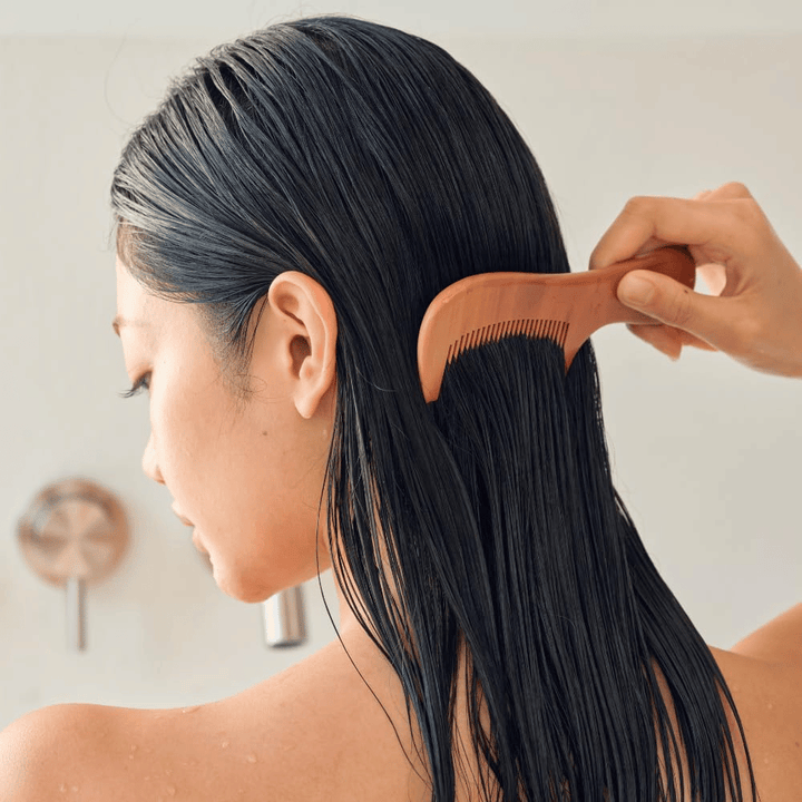 Person grer gjennom langt, vått hår med bred kam etter påføring av Heveblue Salmon Pullkeratin Centella Hair Treatment. Illustrerer en utredende og mykgjørende effekt for et glattere resultat.