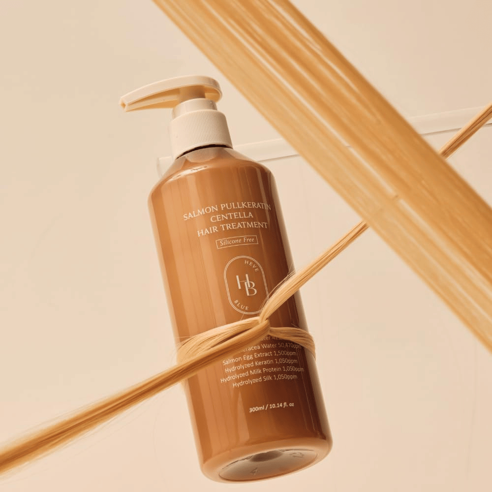 Heveblue Salmon Pullkeratin Centella Hair Treatment i brun flaske omgitt av hårstrå. Bildet fremhever hårbehandlingens pleiende egenskaper med fokus på glans, styrke og silkemykt hår.