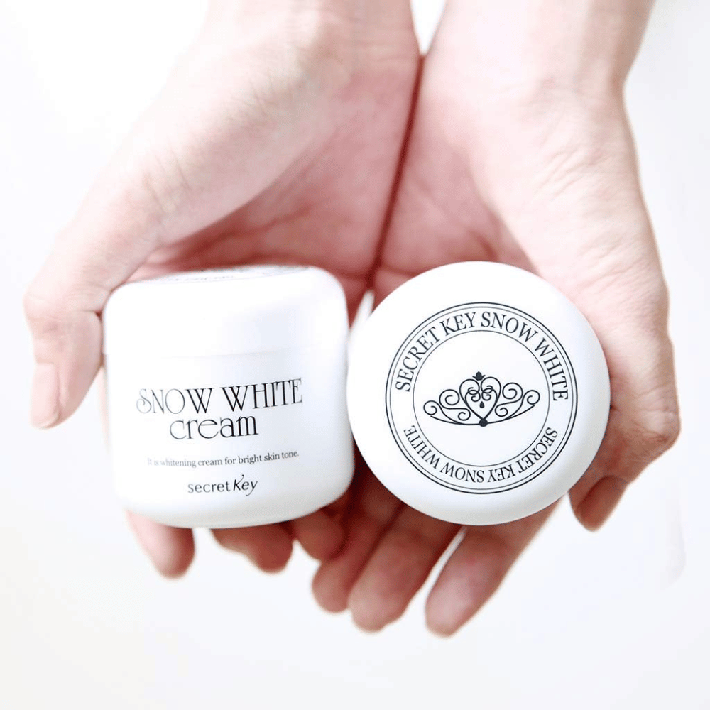 To bokser Secret Key Snow White Cream holdes i hendene, en viser lokket og en viser forsiden.