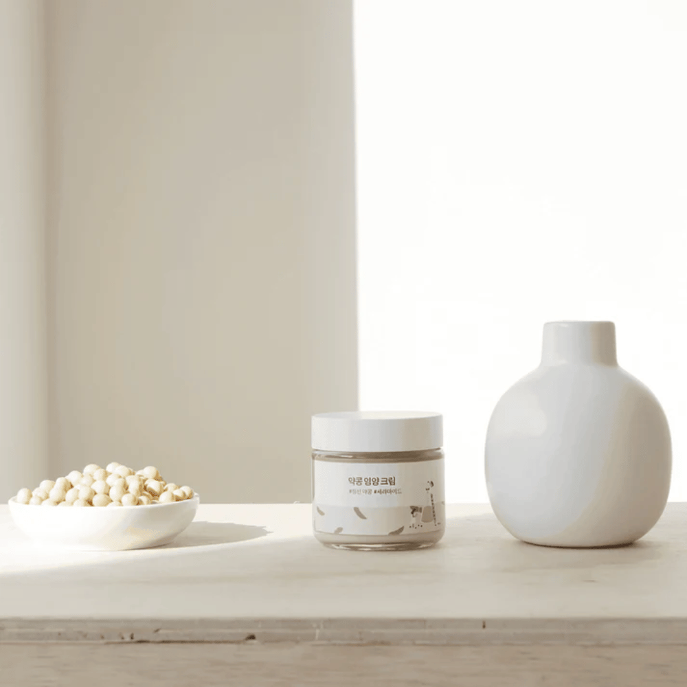 Mixsoon Soybean Nourishing Cream står på et trebord ved siden av en vase og soyabønner. En minimalistisk, fuktighetsgivende krem med naturlige ingredienser.