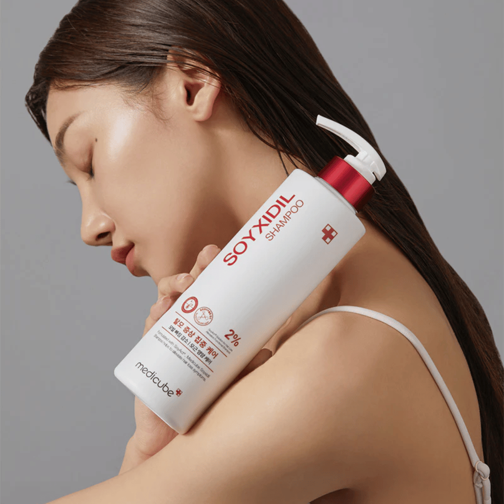 Kvinne med langt hår lener hodet mot en flaske Medicube Soyxidil Shampoo, som styrker hodebunnen og motvirker håravfall.