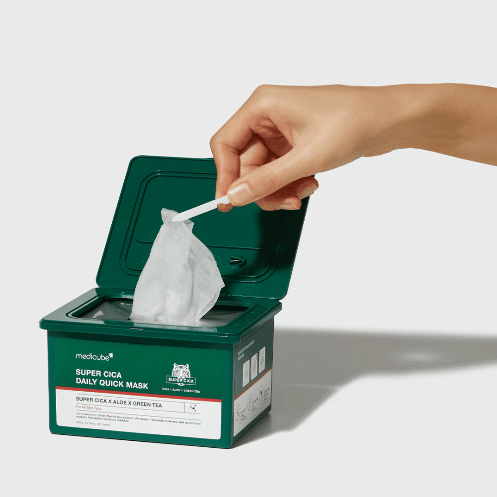 Grønn beholder med åpent lokk viser medicube Super Cica Daily Quick Mask. En hånd trekker opp en arkmask med medfølgende pinsett. Produktet inneholder Cica, aloe og grønn te, ideell for rask fuktighet og beroligende effekt.