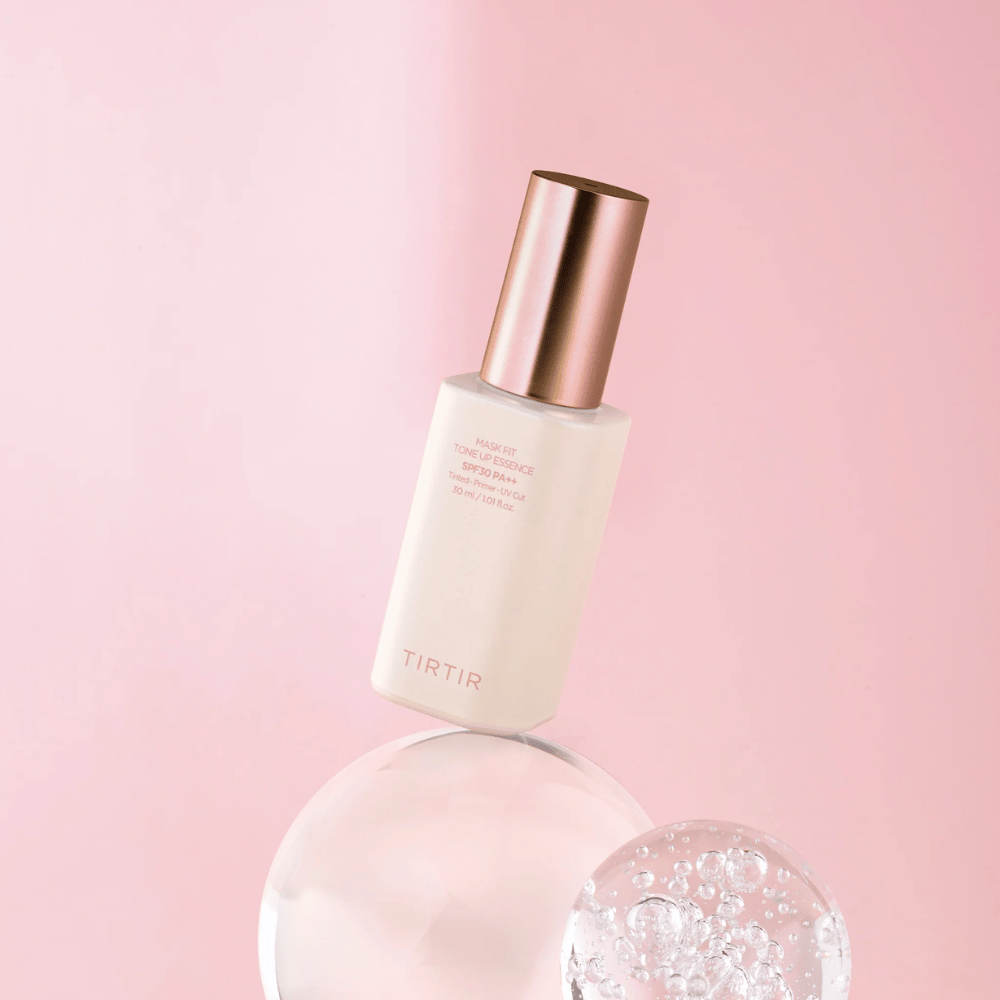 Bildet viser en flaske "TIRTIR MASK FIT TONE UP ESSENCE" med SPF30 PA++ mot en rosa bakgrunn, som gir en følelse av mykhet og femininitet.