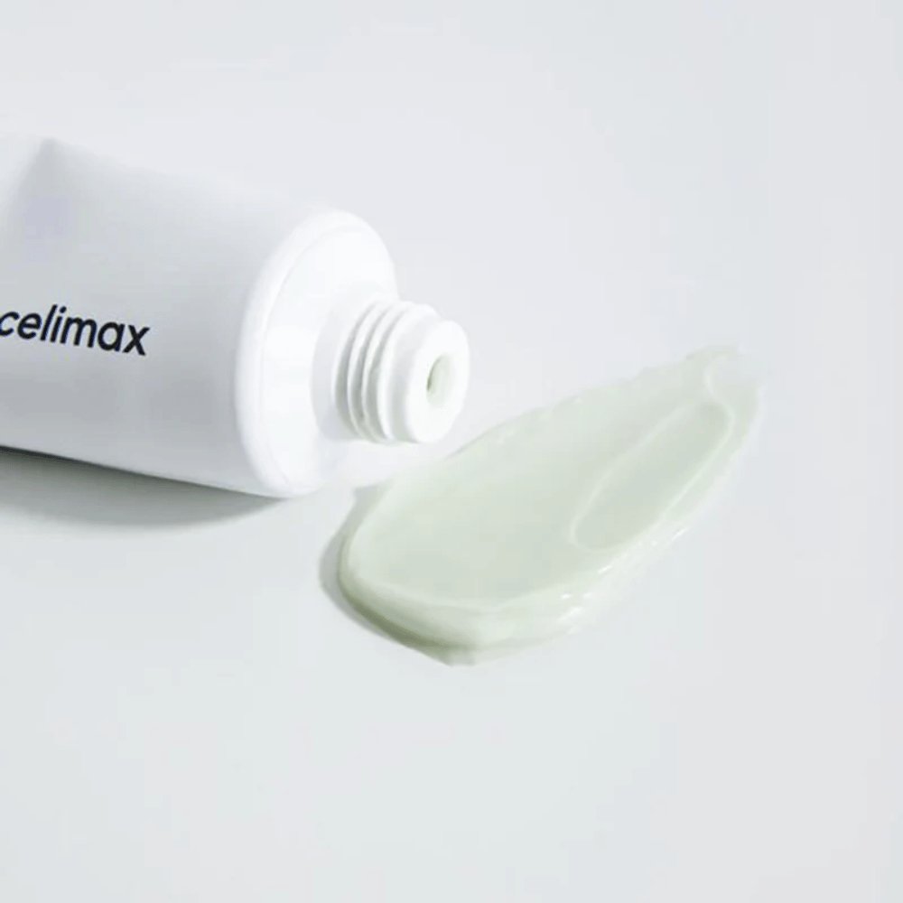Celimax Noni Energy Repair Cream i en hvit tube med en liten mengde lysegrønn krem sprutet ut ved siden av tuben på en hvit overflate. Kremen er for å gi næring og reparere huden.