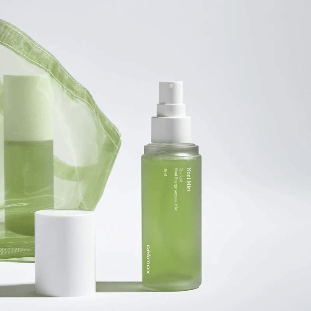 En flaske med Celimax Noni Mist, en grønn sprayflaske med hvit pumpe, som står ved siden av et lokk. Produktet er pakket i en gjennomsiktig plastpose og markedsføres som Noni Energy Ampule Mist.
