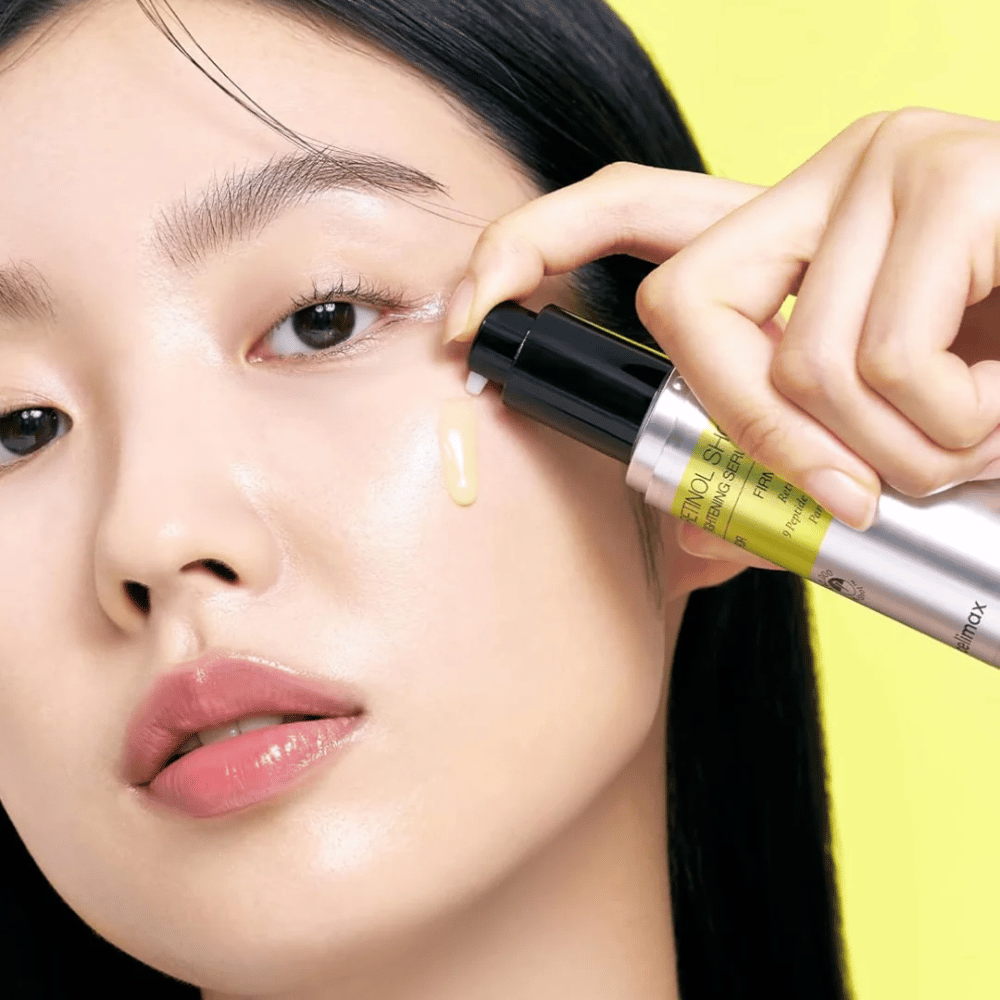 Modell påfører The Vita-A Retinol Shot Tightening Serum fra Tiam nær øyeområdet, med fokus på hudens glød og serumets gule konsistens.