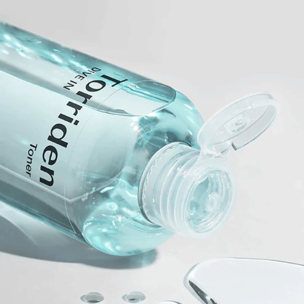 En flaske DIVE-IN Low Molecule Hyaluronic Acid Toner 300ml ved siden av et glass vann, fremmer Torriden og hydrering.