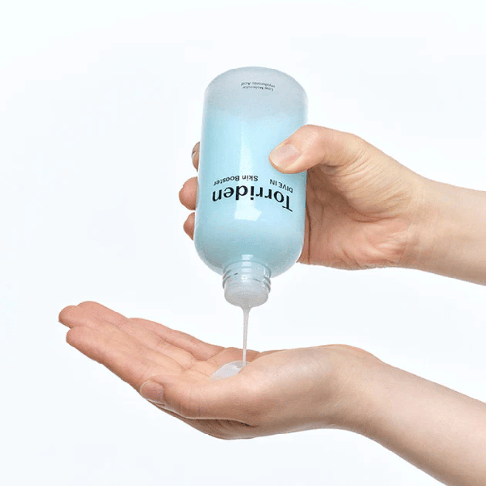Hender som holder en flaske med hudpleieprodukt og doserer ut en klar væske i håndflaten. Flasken er merket med "Torriden - DIVE-IN Low Molecule Hyaluronic Acid Skin Booster".