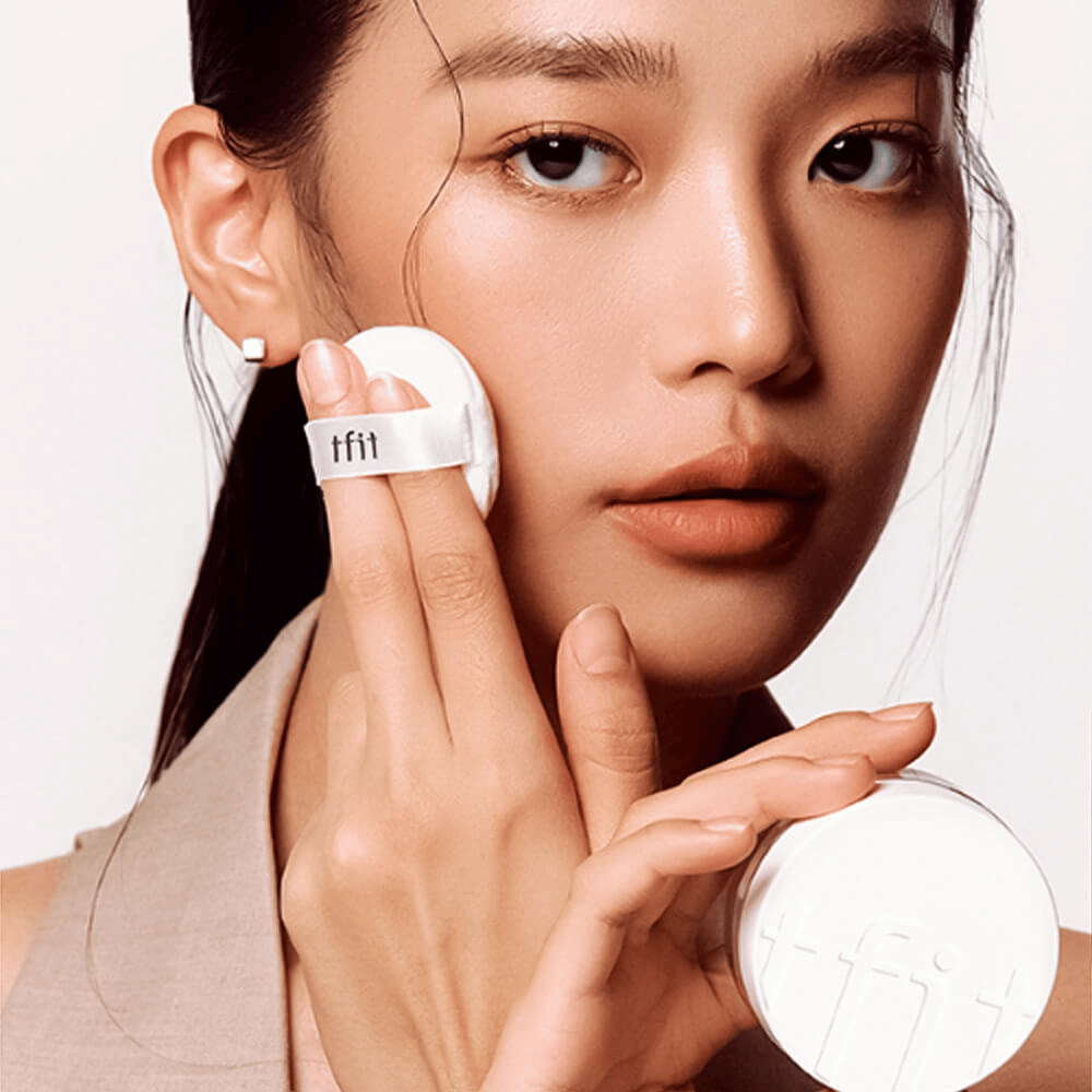 Kvinne påfører TFIT Translucent Set Finishing Powder #02 Skin Beige med en puff, holder i en hvit pudderboks med TFIT-logo.