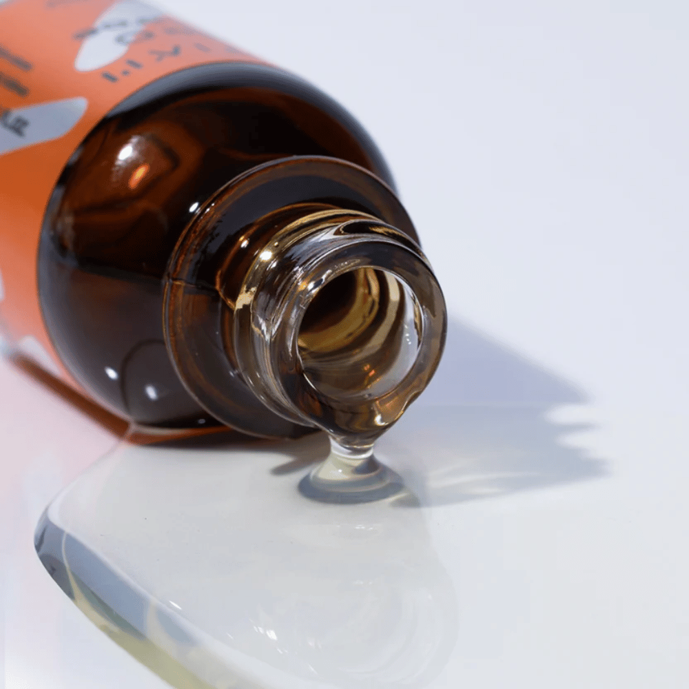Nærbilde av TIA'M Vita C Source-serum som renner ut av en brun glassflaske. Serumets klare formel fremhever dets konsentrerte C-vitamininnhold for en strålende hud.