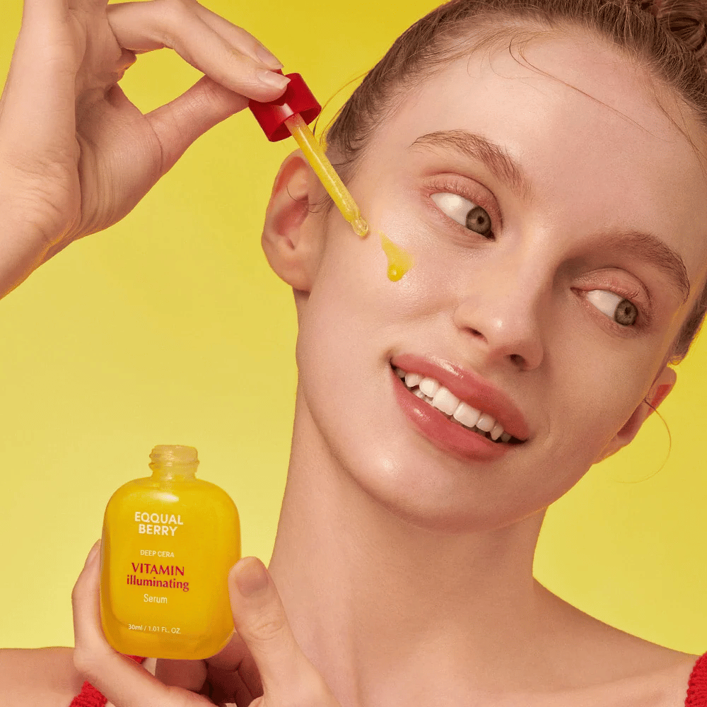Smilende kvinne påfører Equal Berry Vitamin Illuminating Serum med en pipette. Frisk og strålende hud mot en livlig gul bakgrunn som matcher serumets farge.