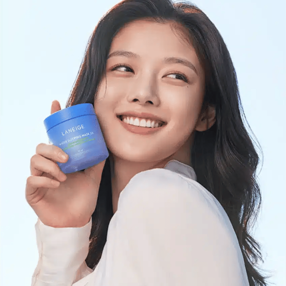 Smilende kvinne holder opp en blå boks av LANEIGE Water Sleeping Mask foran lyseblå bakgrunn.