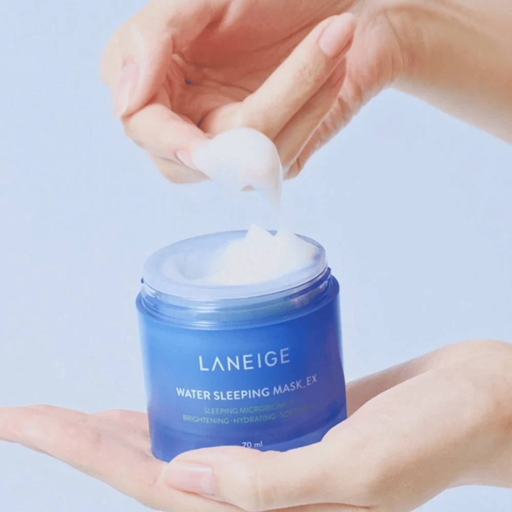 En hånd øser opp LANEIGE Water Sleeping Mask fra en blå boks, med fokus på den gelélignende konsistensen mot lyseblå bakgrunn.
