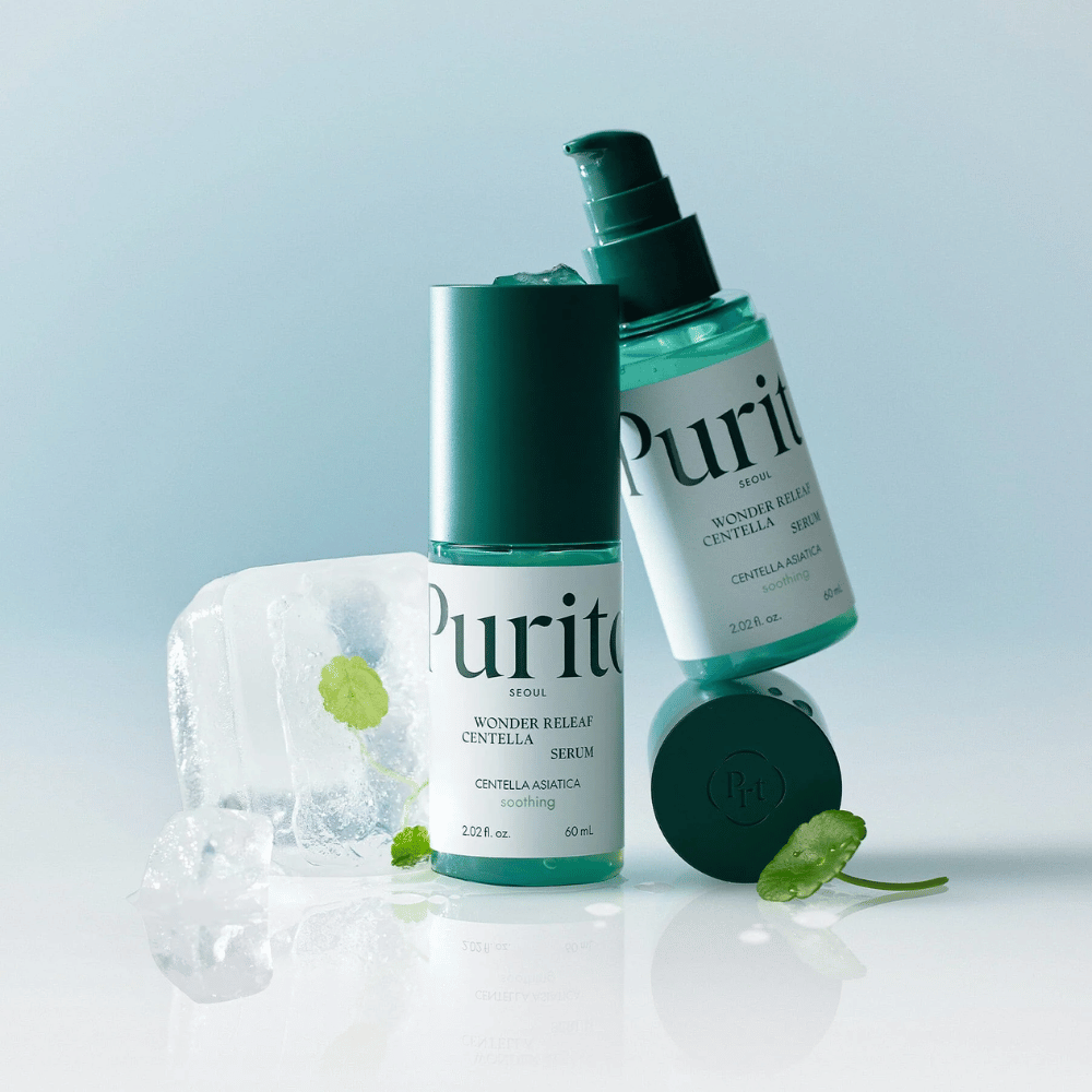 To flasker av Purito Wonder Releaf Centella Serum, en stående og en liggende, omgitt av isbiter med centellablader inni samt et løst blad på en lyseblå overflate.