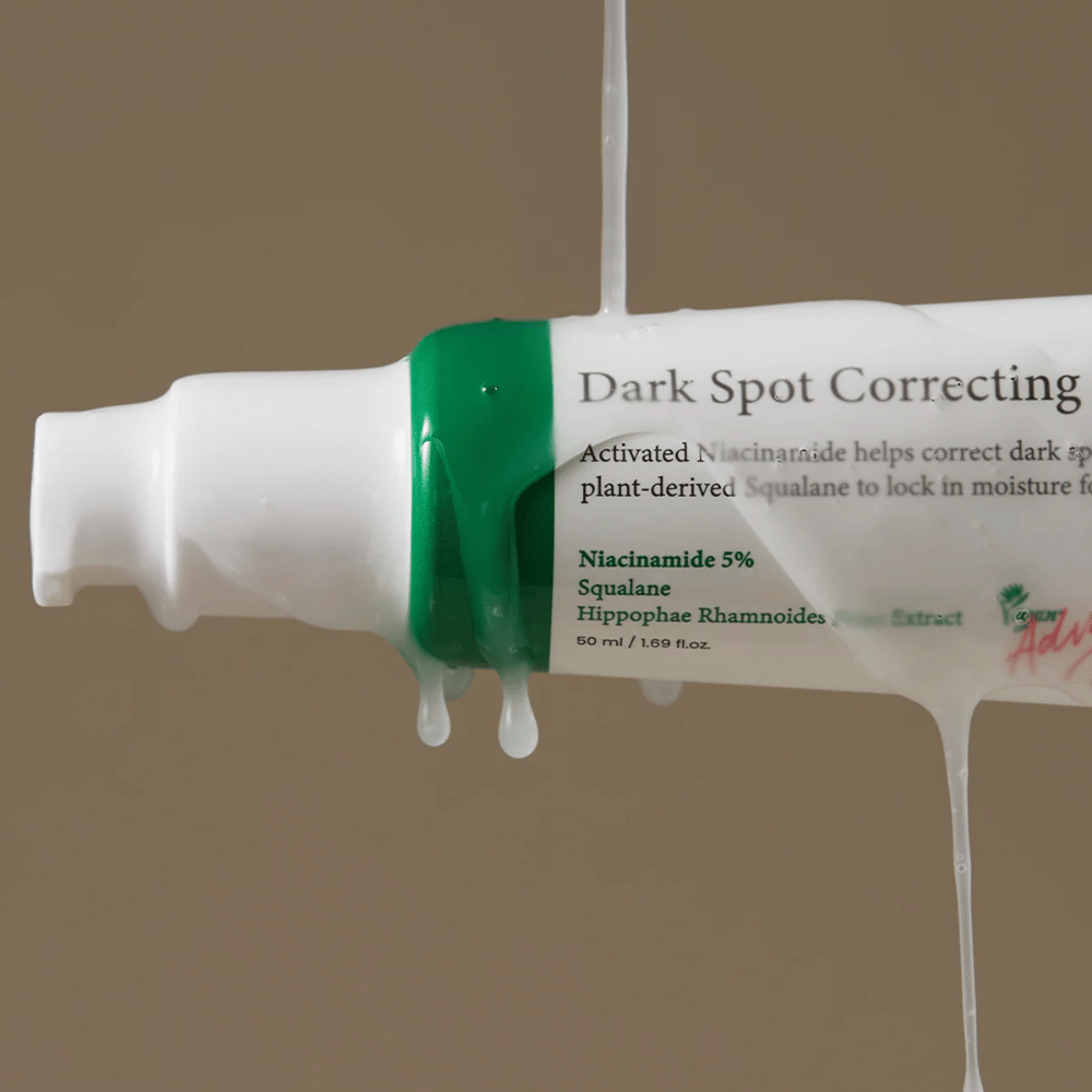 Nærbilde av en pumpeflaske av Axis-Y Dark Spot Correcting Glow Serum med hvit emballasje og grønn kork, dekket av rennende gjennomsiktig væske.