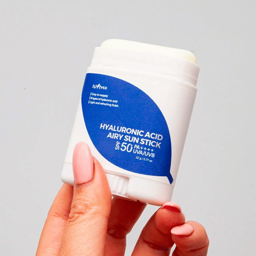 En hånd holder i en hvit solstikk med blå etikett fra merket Isntree. Produktet heter "Hyaluronic Acid Airy Sun Stick" og har solbeskyttelsesfaktor SPF 50+ PA++++.