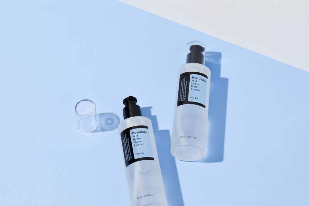 COSRX:s Hyaluronic Acid Hydra Power Essence 100ml gir fuktighetsgivende fordeler på blå overflate.