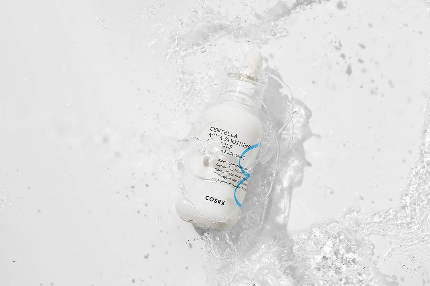En flaske COSRX Centella Aqua Soothing Ampoule 40ml som spruter på en hvit overflate, reduserer rødhet og gir beroligende fuktighet.