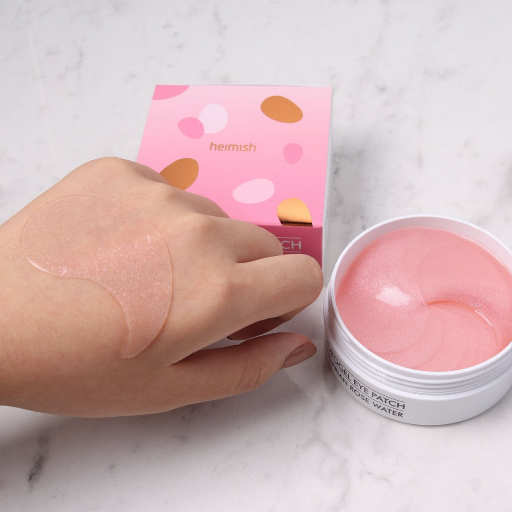 En hånd som holder en rosa Bulgarian Rose Hydrogel Eye Patch 60stk fra heimish og påfører øyemaske.