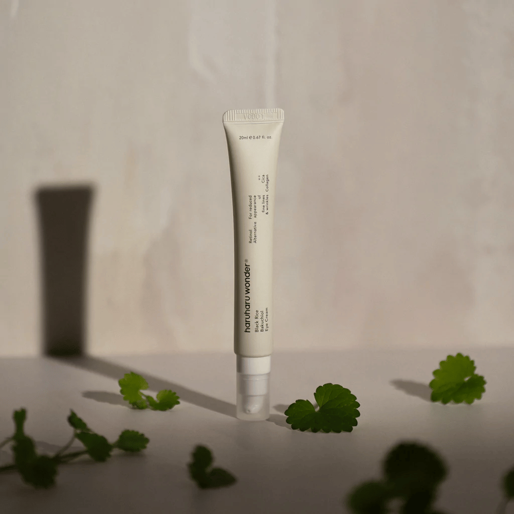 En tube Haruharu Wonder Black Rice Bakuchiol Eye Cream 20ml omgitt av grønne blader, rettet mot synligheten av rynker og fine linjer.