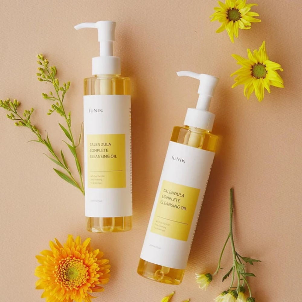 To flasker iUNIK Calendula Complete Cleansing Oil 200ml med gule blomster på beige bakgrunn, infundert med planteolje.