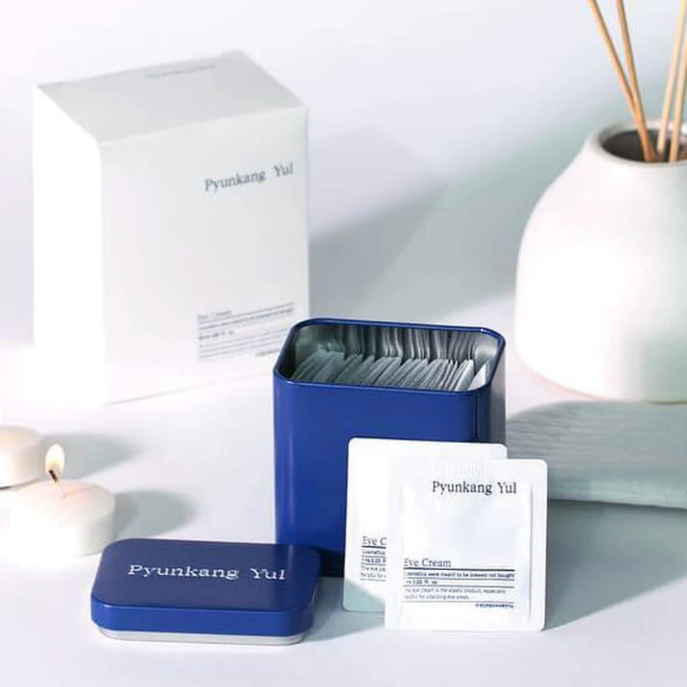En hvit eske med blått lokk og Pyunkang Yul Eye Cream 1ml x 50stk ved siden av.