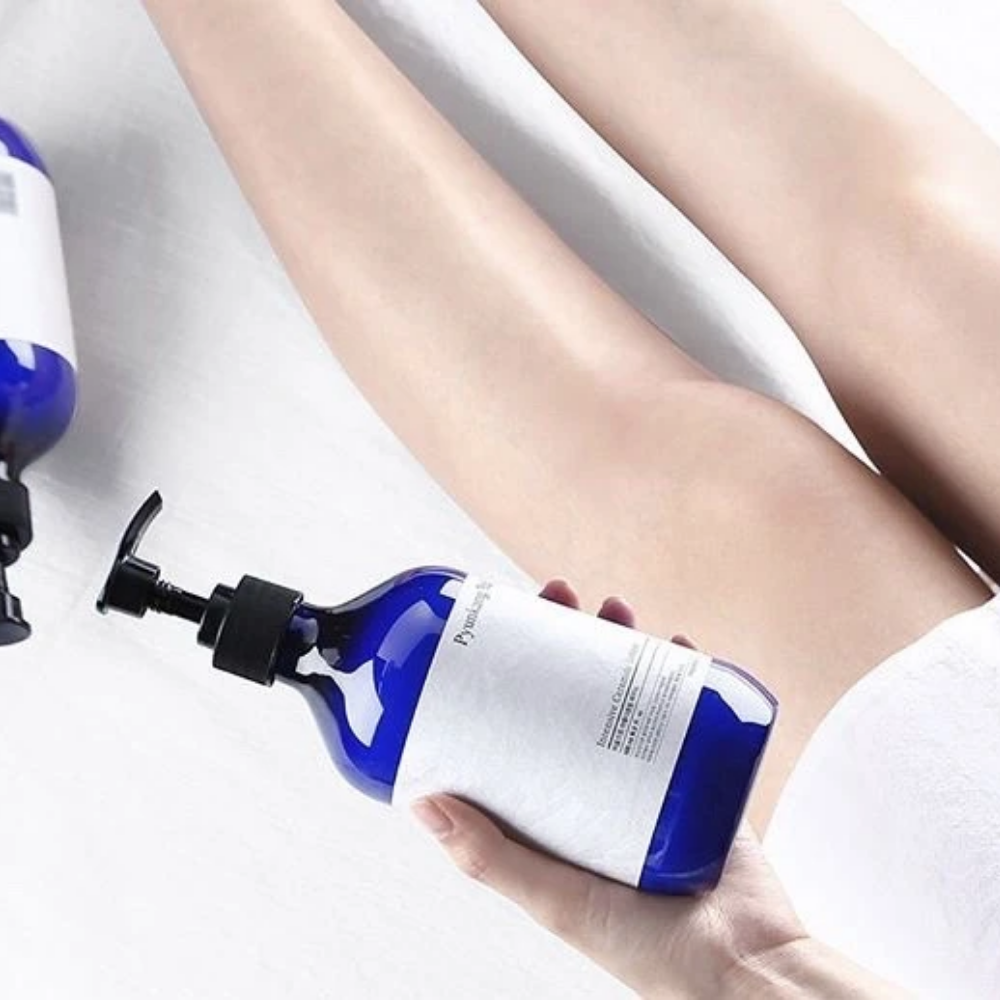 En kvinne som holder en flaske Pyunkang Yul Intensive Ceramide Lotion 500ml ved siden av bena sine.