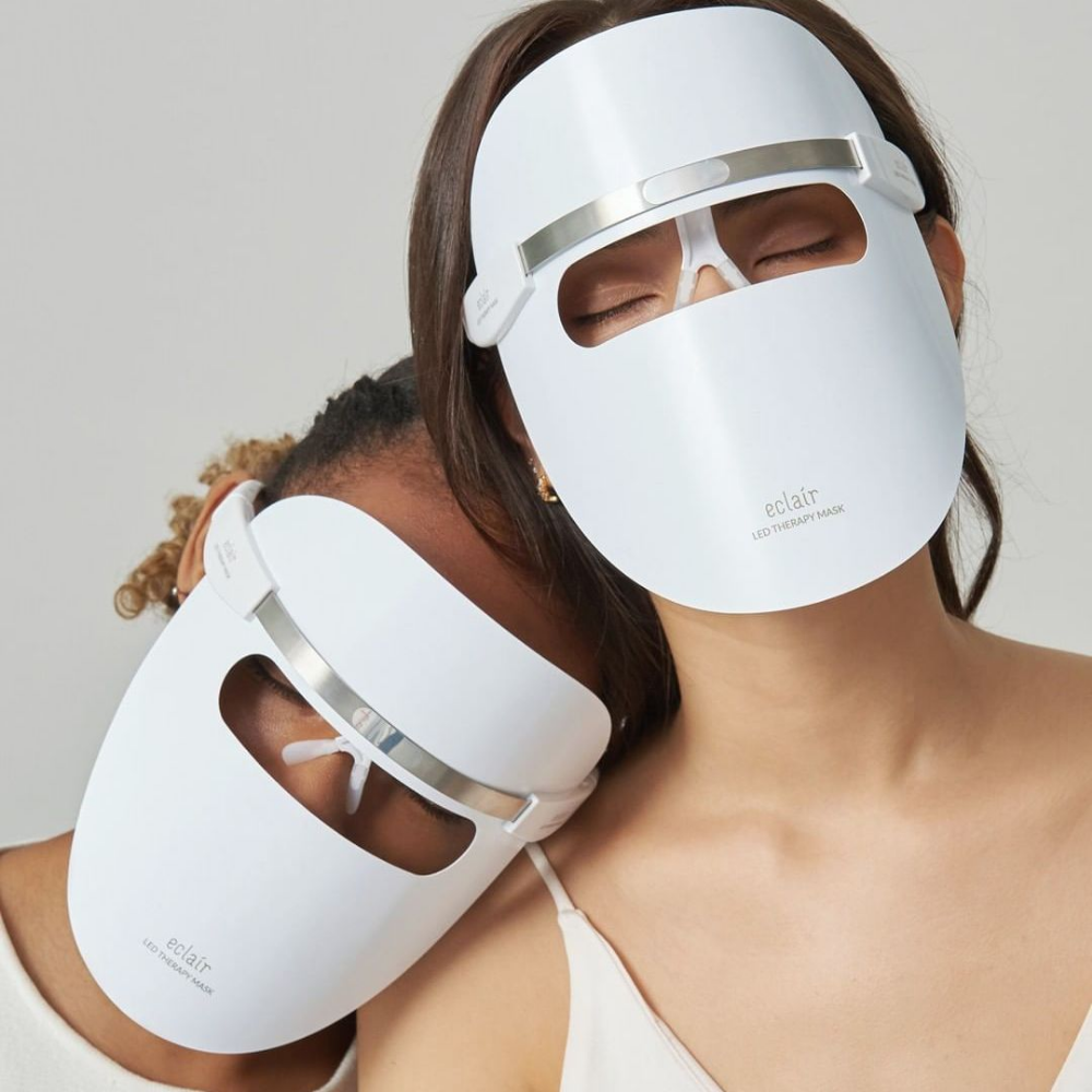 To kvinner som bærer hvite masker demonstrerer ECLAIR LED Therapy Mask for hudtonen forbedringer.