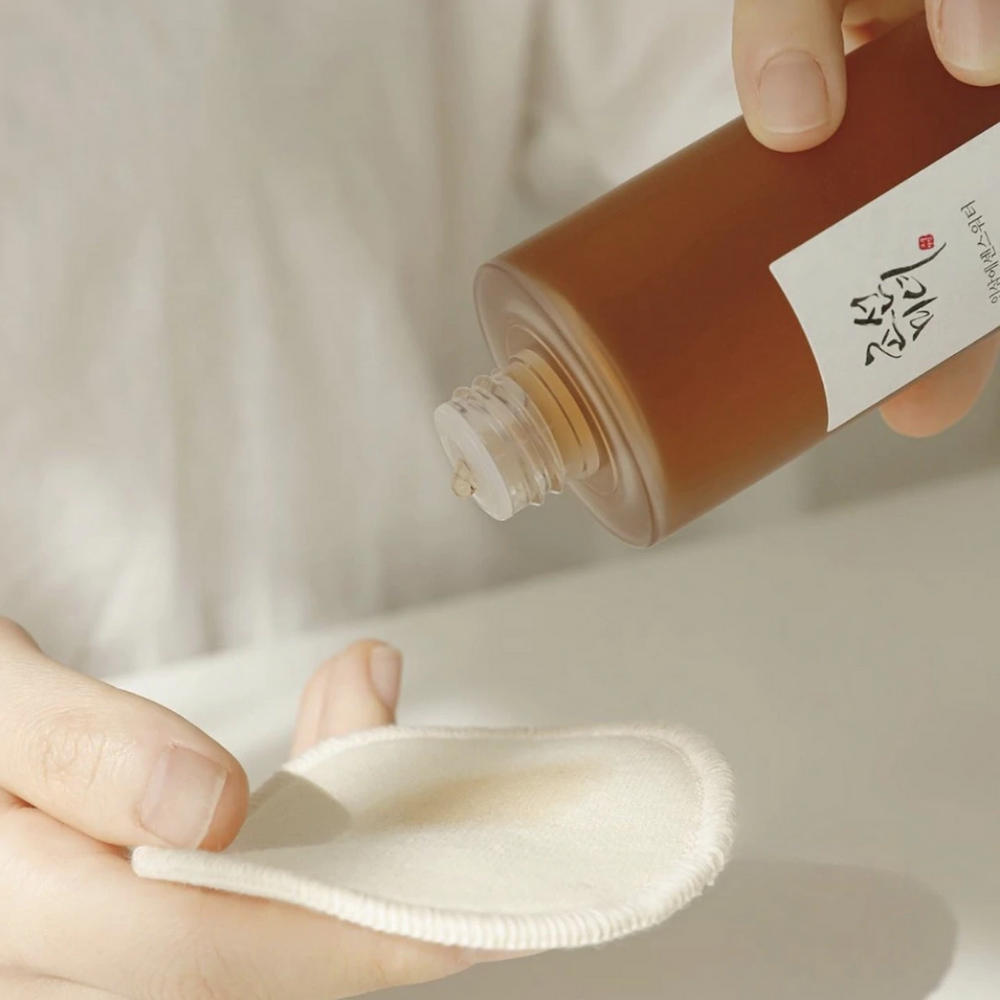 En person som heller Beauty of Joseon Ginseng Essence Water 150ml på en klut for å ta hånd om tørr hud og redusere talgproduksjon.